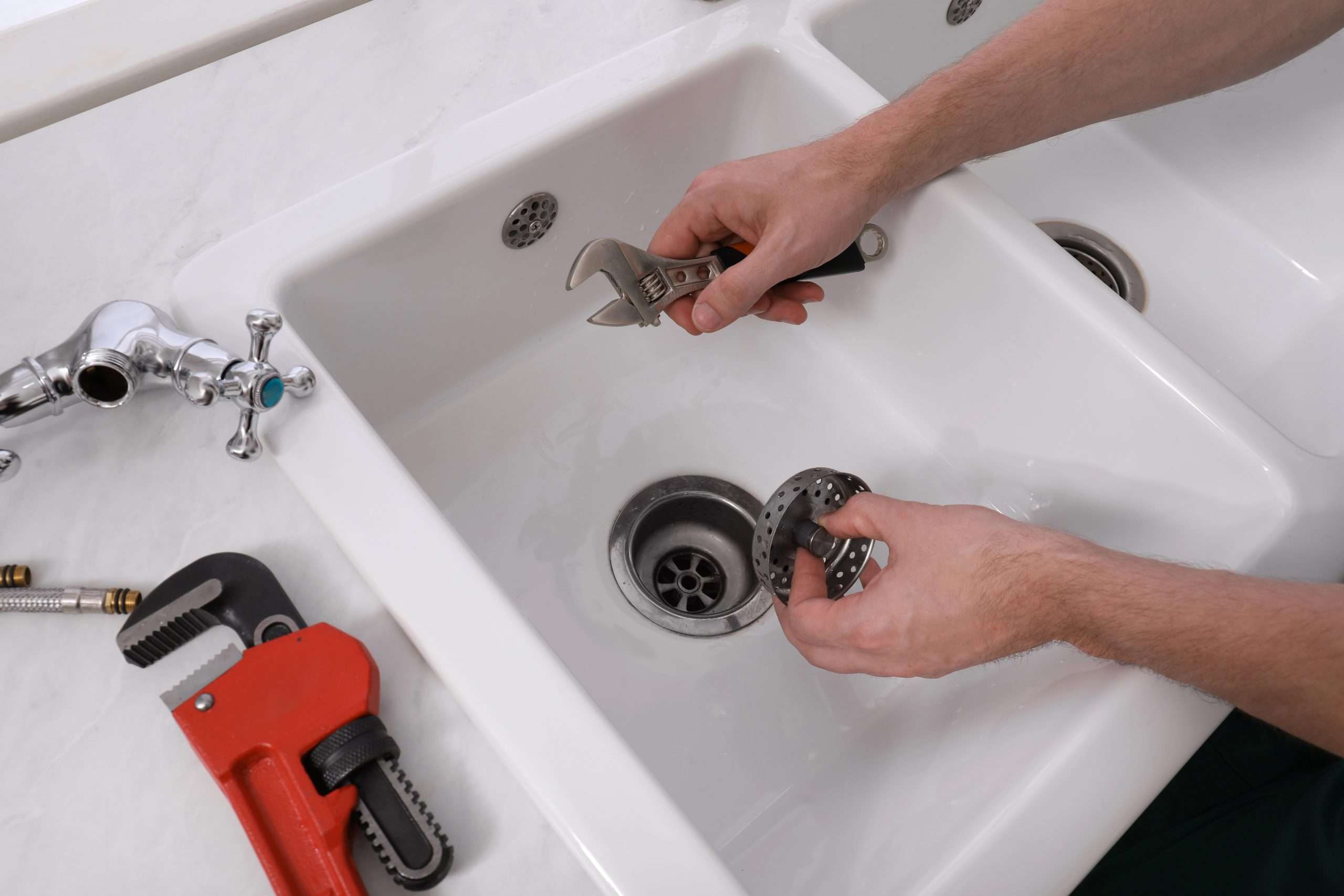 Plumber removing a sink drain strainer with a wrench during kitchen drain cleaning.